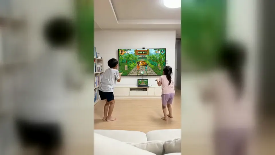 Two kids tiptoeing in front of a TV, sneaking up on a sleeping tiger on screen